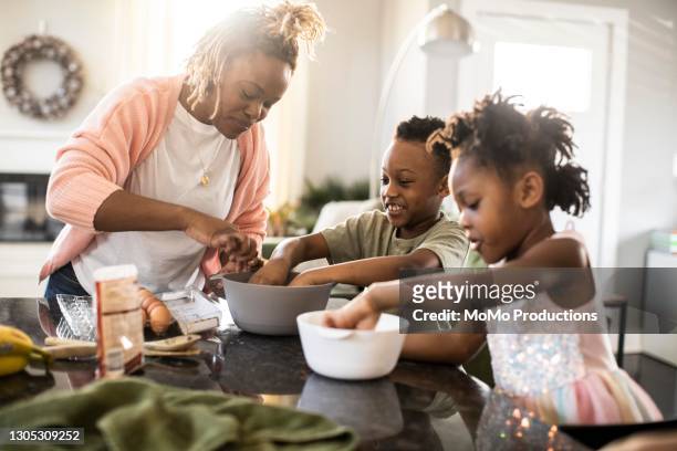 family mixing cookie dough at home - mother and daughter cooking photos et images de collection