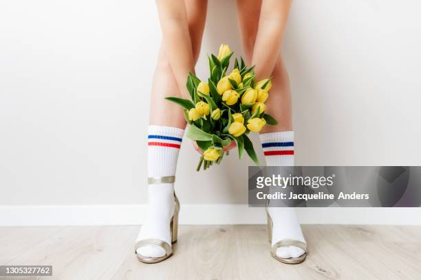 woman wearing sport socks in high heels holding yellow tulips - fashion oddities stock pictures, royalty-free photos & images