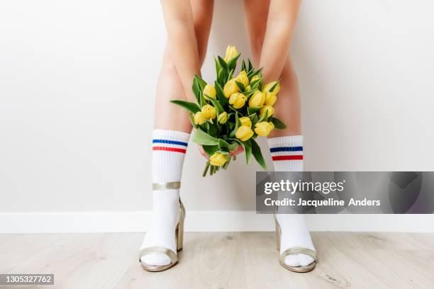 woman wearing sport socks in high heels holding yellow tulips - acessórios de moda imagens e fotografias de stock