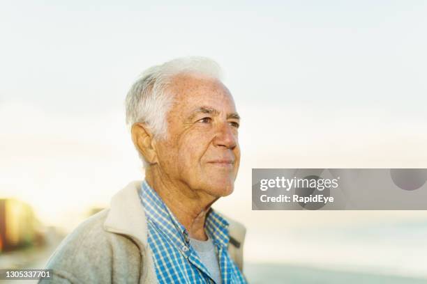 senior man with white hair stands beside the sea at sunrise, lost in thought - horizon brightly lit stock pictures, royalty-free photos & images