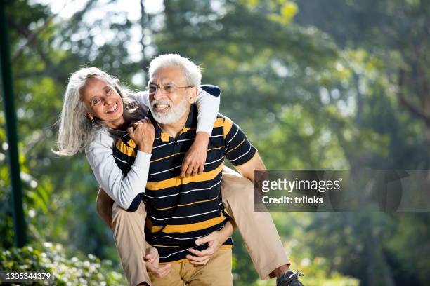 senior man piggybacking his wife - couple stock pictures, royalty-free photos & images