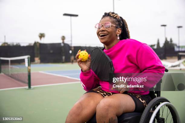 jonge zwarte gehandicapte vrouw in rolstoel die pickleball met vriend speelt - disabilitycollection stockfoto's en -beelden