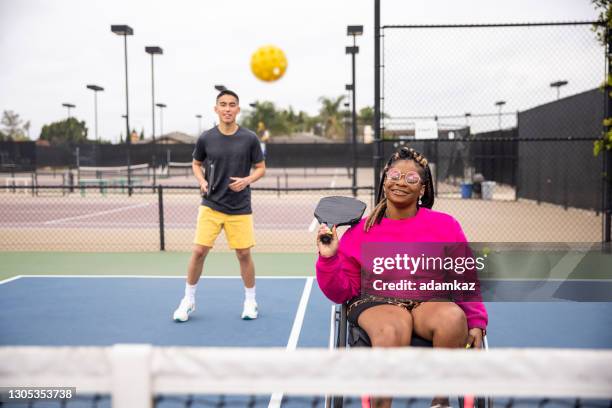 junge schwarze behinderte frau im rollstuhl spielen pickleball mit freund - paddle tennis stock-fotos und bilder