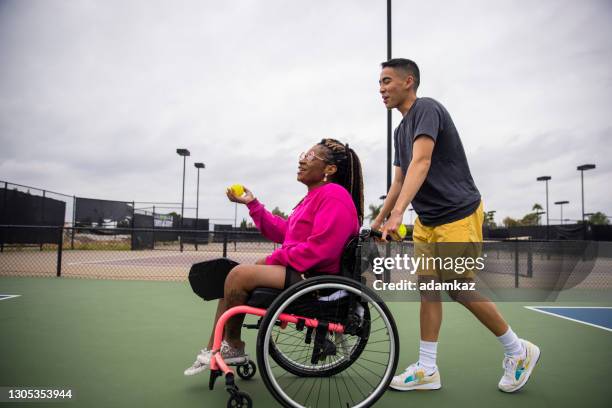 young black disabled woman in wheelchair playing pickleball with friend - pushing wheelchair stock pictures, royalty-free photos & images