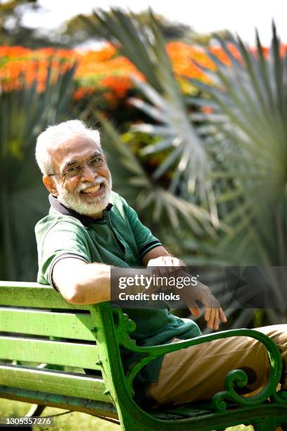 happy senior man spending leisure time sitting at park bench - garden bench stock pictures, royalty-free photos & images