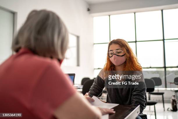 teacher grading tests and talking to student - wearing face mask - employee engagement mask stock pictures, royalty-free photos & images