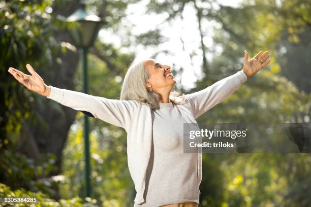 senior woman with arms outstretched at park - enjoyment stock pictures, royalty-free photos & images