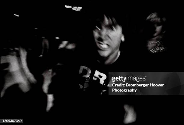 View of a young skinhead, his teeth clenched as he run through a crowd at an unspecified club, Santa Clara, California, 1987. He wears shirt...
