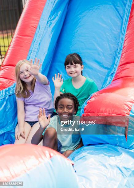 kinder auf riesigen aufblasbaren rutsche, mädchen mit daunen - inflatable playground stock-fotos und bilder