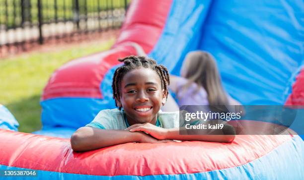 african-american boy playing on giant inflatable slide - inflatable playground stock pictures, royalty-free photos & images