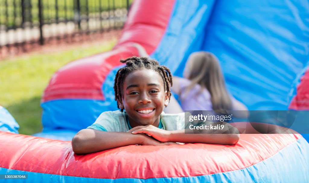 非洲裔美國男孩在巨大的充氣滑梯上玩耍