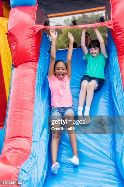 two girls playing on giant inflatable slide - inflatable playground stock pictures, royalty-free photos & images