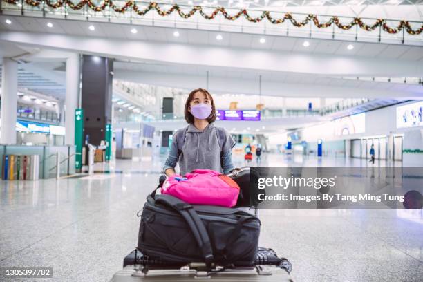 young asian woman in protective face mask pushing a luggage cart to the check-in counter in airport terminal - coronavirus airport stockfoto's en -beelden