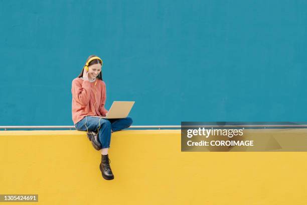 young woman using a laptop and headphones outdoors. - laptop coloured background stock pictures, royalty-free photos & images