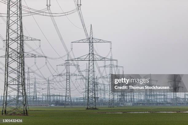 network of power lines with power wires and pylons, cloudy sky as background, view from below - hochspannungsmast stock-fotos und bilder