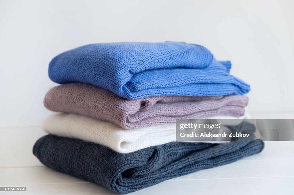 Knitted woolen things of different colors, stacked in a pile, lie on a white wooden table. Winter and autumn warm cozy sweaters for charity. The concept of storage, care and washing of handmade products.