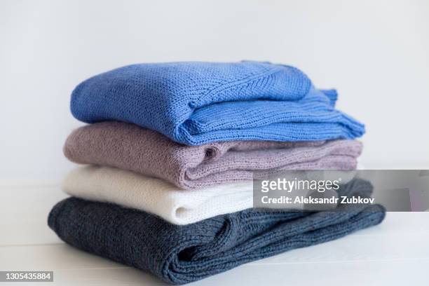 knitted woolen things of different colors, stacked in a pile, lie on a white wooden table. winter and autumn warm cozy sweaters for charity. the concept of storage, care and washing of handmade products. - top garment stock pictures, royalty-free photos & images