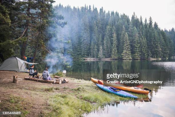two female friends sitting next to campfire in a wild camp in the mountain. - camping equipment stock pictures, royalty-free photos & images