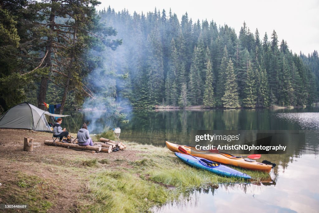 Two female friends sitting next to campfire in a wild camp in the mountain.