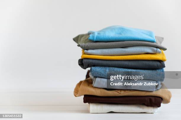 a stack of things on a white table or background, indoors. clean folded cotton denim clothing and bright colored t-shirts. the concept of housework, ironing, care and storage of things. copy of the text space. - clothes wardrobe stockfoto's en -beelden