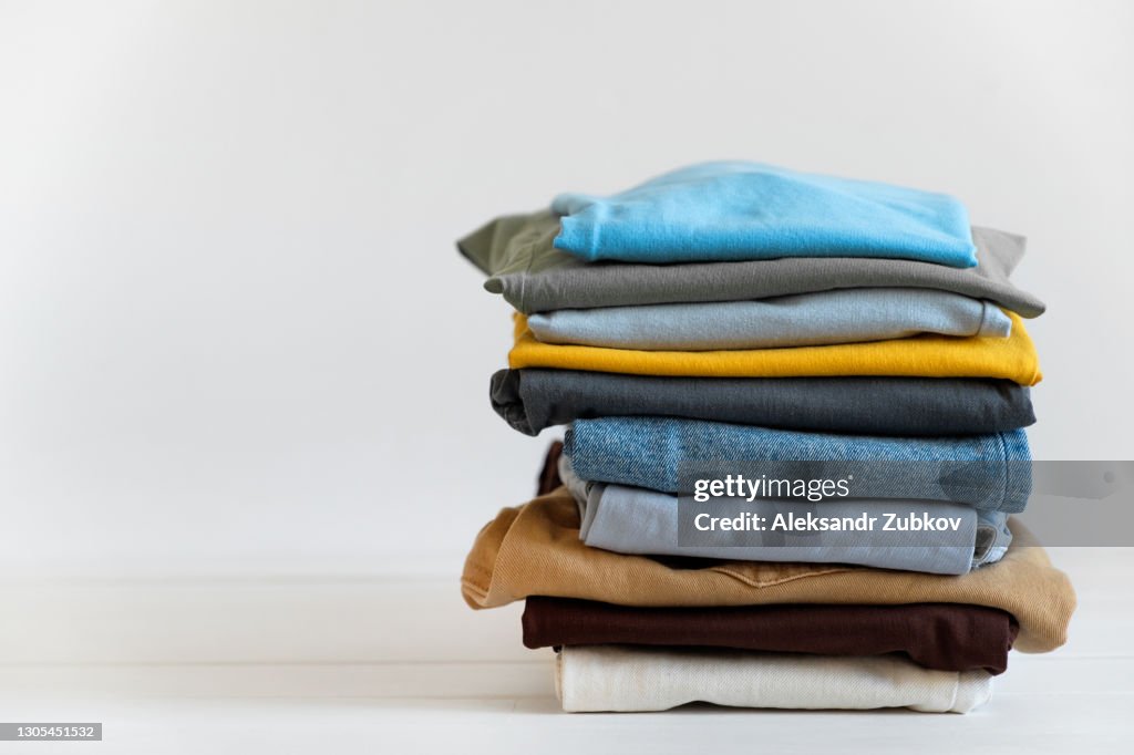 A stack of things on a white table or background, indoors. Clean folded cotton denim clothing and bright colored T-shirts. The concept of housework, Ironing, care and storage of things. Copy of the text space.