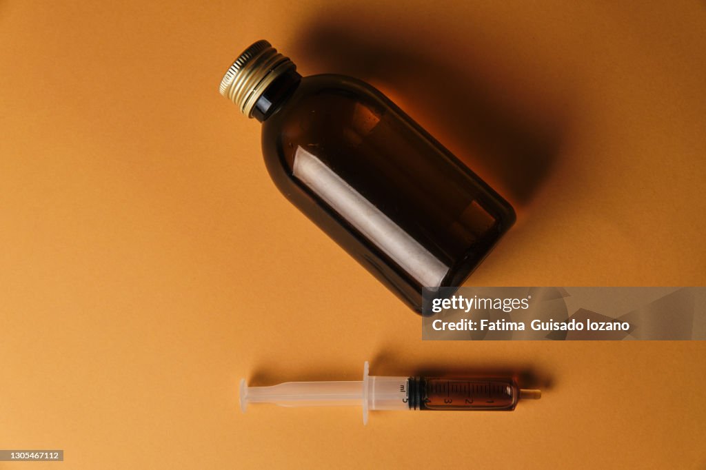 Bottle of cough syrup on yellow background with its syringe for drinking