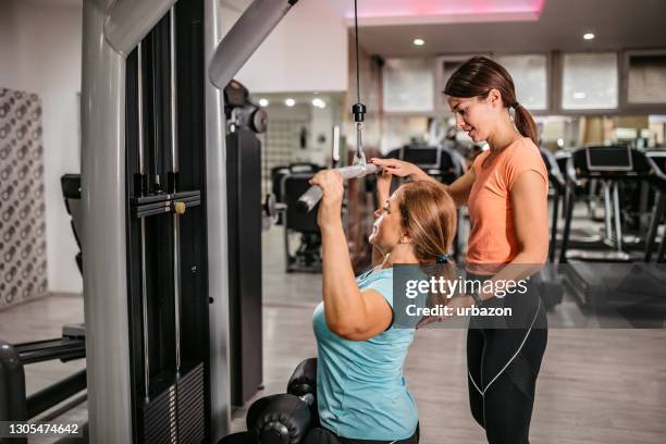 seniorin macht lat pulldowns mit trainern hilfe - fitness trainer stock-fotos und bilder
