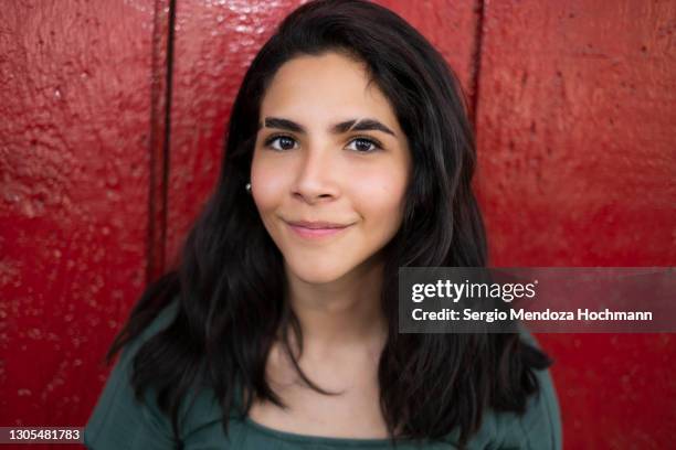 young latino woman smiling at the camera and standing against a red wooden door in mexico city - eyebrow slit fotografías e imágenes de stock