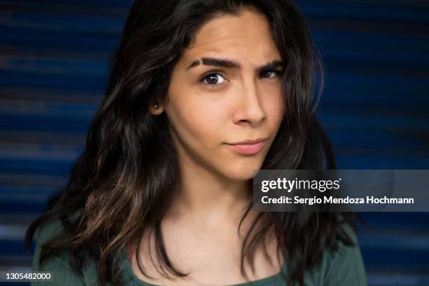 young latino woman with a blue background looks curiously at the camera in mexico city, mexico - raised eyebrows imagens e fotografias de stock