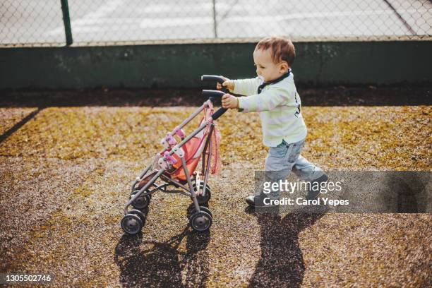 baby boy push doll stroller outdoor.he is wearing casual clothes and pacifier - nachahmung erwachsener stock-fotos und bilder