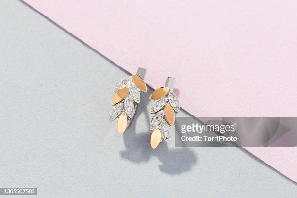 silver and gold earrings in leaves shape decorated with diamonds on pink and gray background - ohrring stock-fotos und bilder
