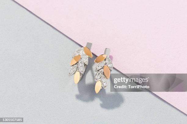 silver and gold earrings in leaves shape decorated with diamonds on pink and gray background - jewellery products stock pictures, royalty-free photos & images