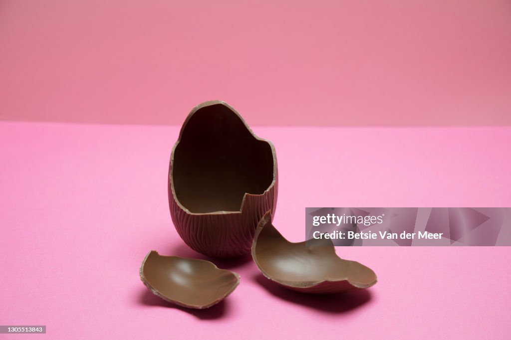 Broken chocolate Easter egg on pink background.