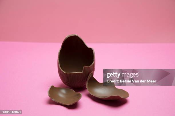 broken chocolate easter egg on pink background. - easter egg stock pictures, royalty-free photos & images