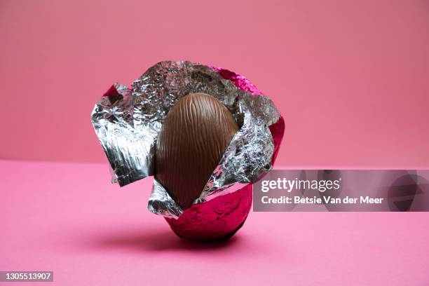 a half unwrapped easter egg on a pink background. - schokolade stock-fotos und bilder