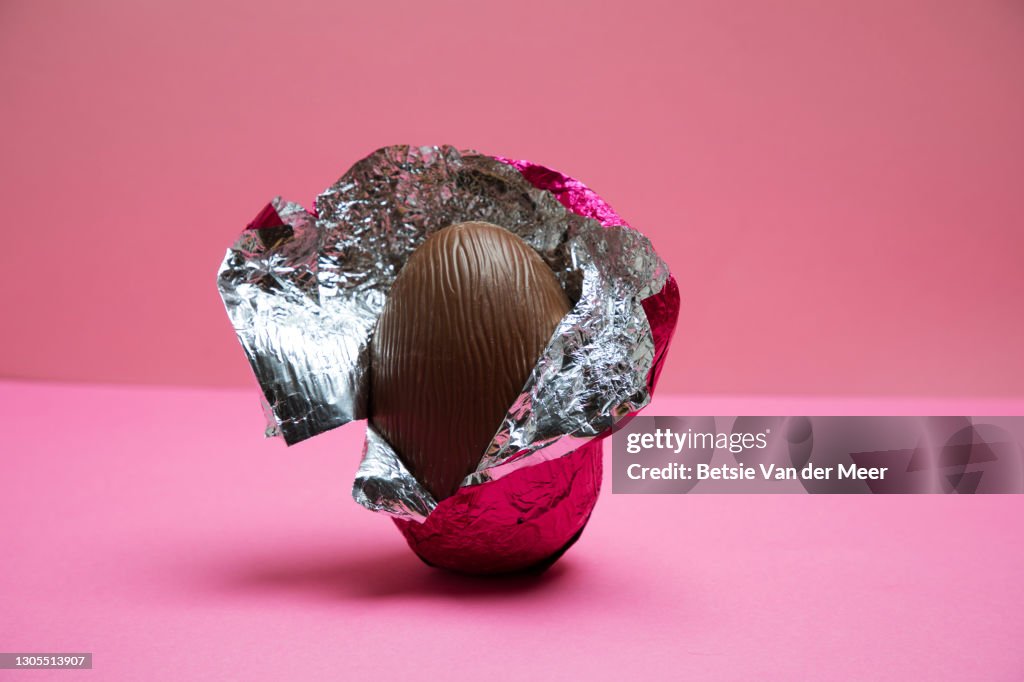 A half unwrapped Easter egg on a pink background.
