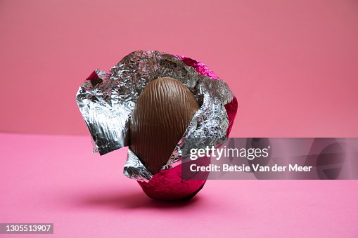 A half unwrapped Easter egg on a pink background. A half unwrapped Easter egg on a pink background.
