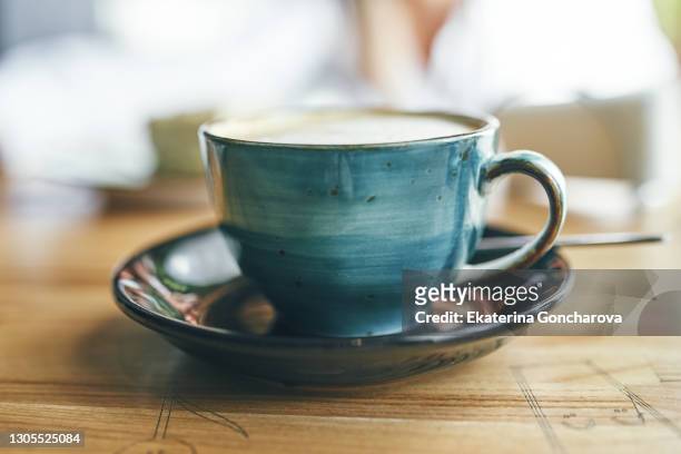 cup of cappuccino with latte on wooden background. beautiful foam, greenery ceramic cups, stylish toning, place for text. coffee in blue cup on wooden table in cafe with lighting background - breakfast top view stock pictures, royalty-free photos & images