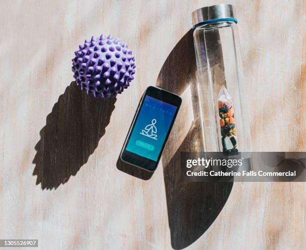 mobile phone displaying a meditation app, beside a water bottle and a spiked massage ball - yoga ball fotografías e imágenes de stock