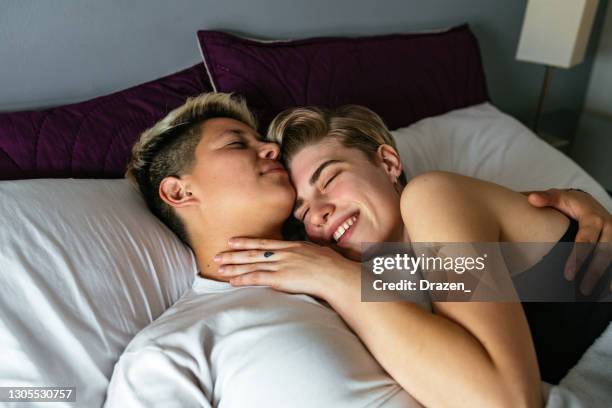 lesbian latino millennial couple in bed, waking up and kissing - romantic young couple sleeping in bed stock pictures, royalty-free photos & images