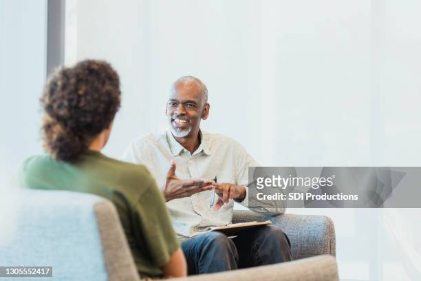 unrecognizable woman listens as cheerful counselor gestures and speaks - psychotherapy imagens e fotografias de stock