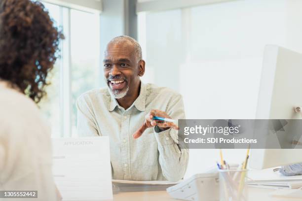 mature male banker smiles and gestures while speaking to customer - bankers imagens e fotografias de stock