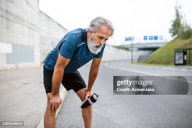 exhausted mature male runner stopping for rest and water - exhausted runner stock pictures, royalty-free photos & images