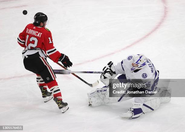 Curtis McElhinney of the Tampa Bay Lightning moves in front of the crease to knock the puck away from Alex DeBrincat of the Chicago Blackhawks at the...