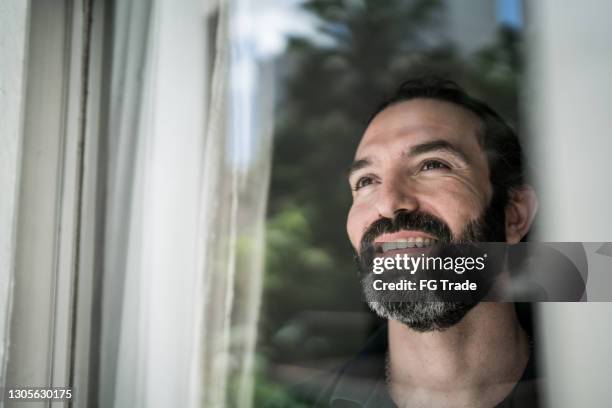 hombre maduro mirando a través de la ventana en casa - humility fotografías e imágenes de stock