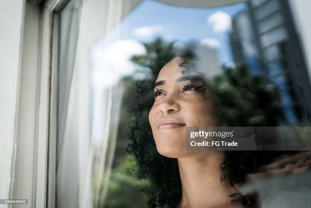 Giovane donna che guarda attraverso la finestra di casa