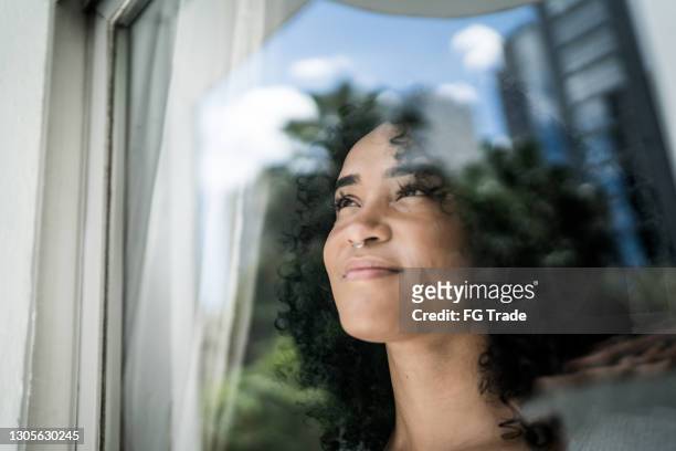 jonge vrouw die door venster thuis kijkt - positieve emotie stockfoto's en -beelden