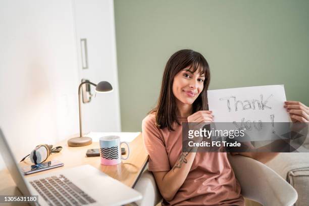 ritratto di una giovane donna a casa che tiene la carta con scritto "grazie" - poster casa foto e immagini stock