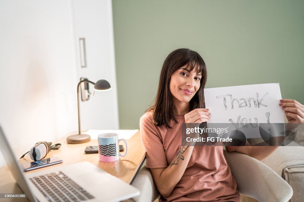 Portret van een jonge vrouw thuis die document met 'dank u' houdt geschreven