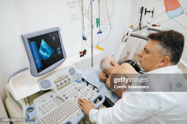 männlicher arzt, der das herz eines patienten mit einem ultraschallgerät untersucht - echokardiogramm stock-fotos und bilder